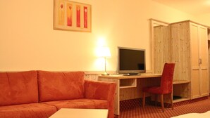 Une chambre d’hôtel comprenant un canapé, un bureau avec une télévision, une chaise et une armoire.