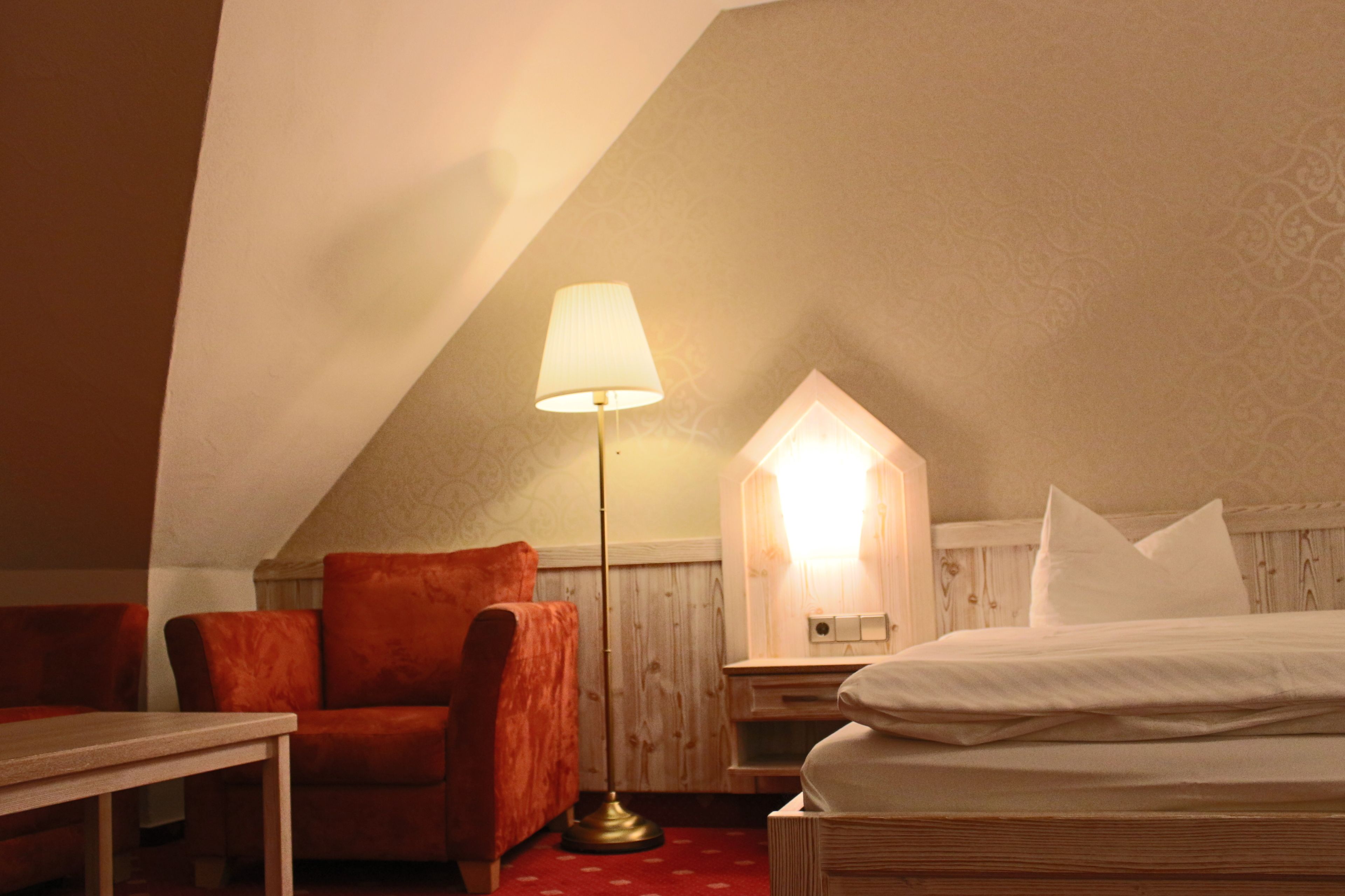 Ein gemütliches Zimmer mit einem Bett, einem Sessel, einer Lampe und einem Holzschrank.