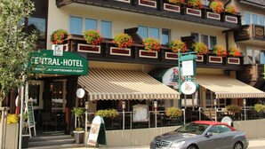 Un hôtel à plusieurs étages, doté de balcons ornés de jardinières fleuries, avec une entrée bien visible et une voiture garée devant.