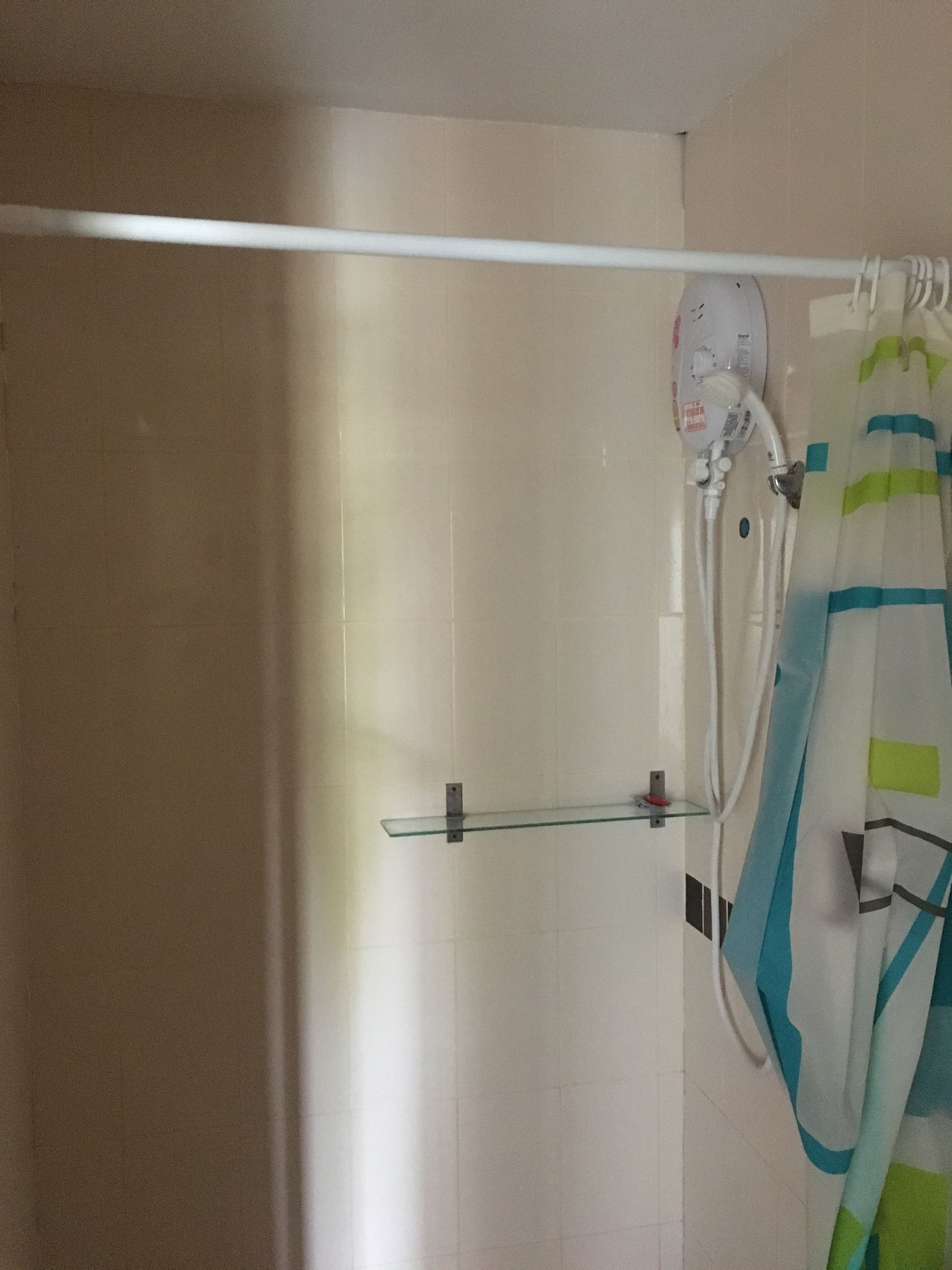 Un baño con cortina de ducha, estante de vidrio y toallero blanco.