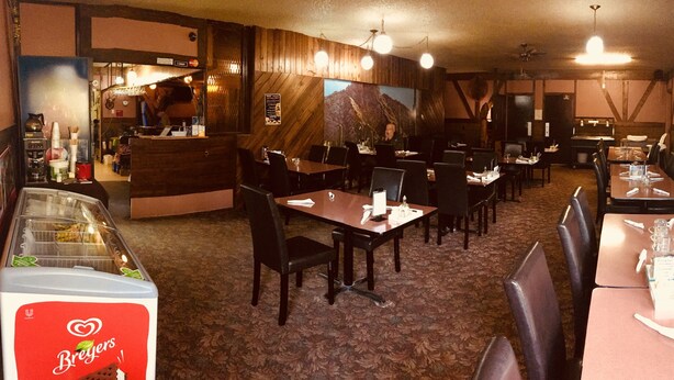 A restaurant interior with wooden walls, multiple tables and chairs, and a Breyers ice cream freezer. - Sharptail Motor (Ashern)