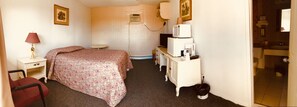 A bedroom with a bed, bedside table, lamp, dresser, and a small window.