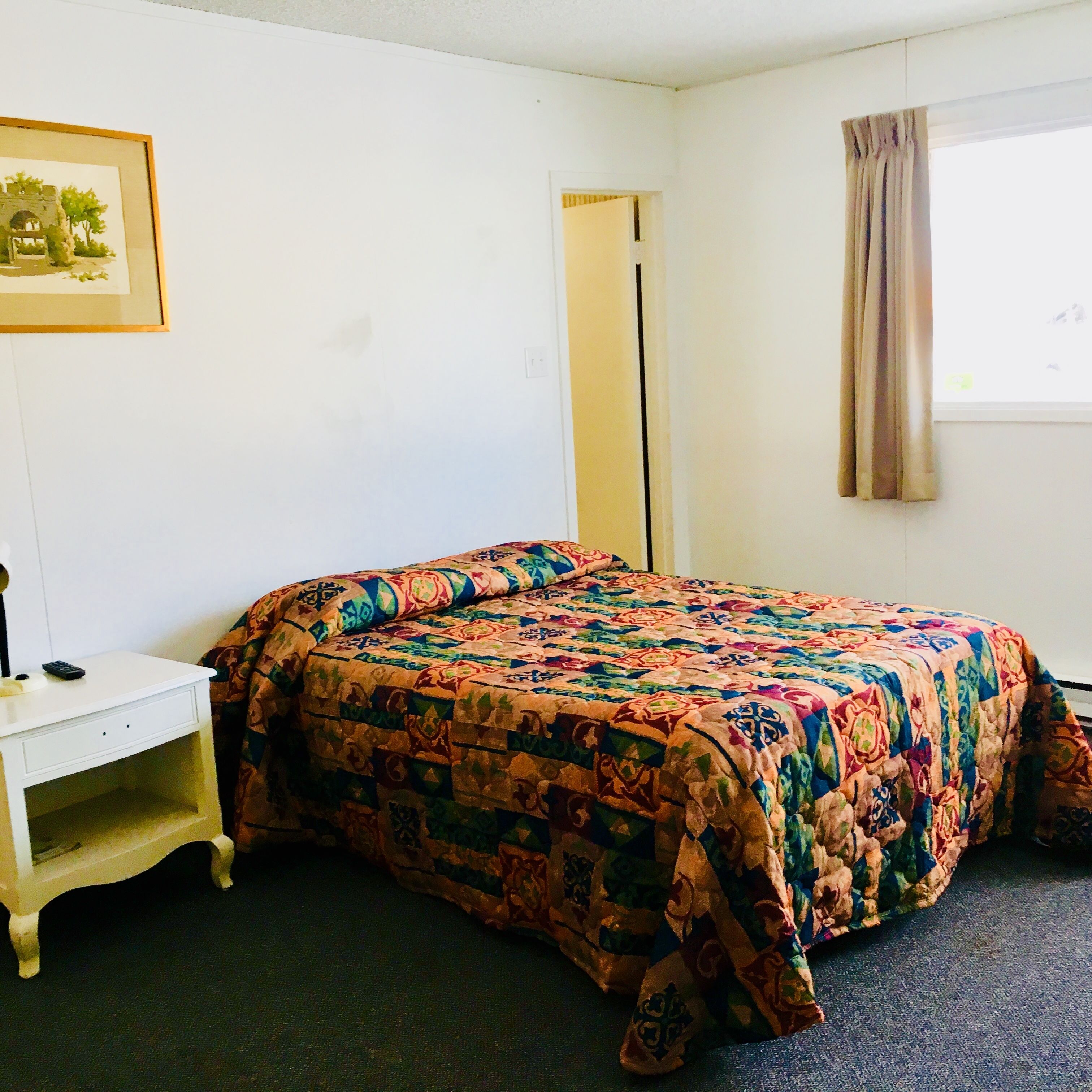 Un letto singolo con una coperta colorata, un comodino con una lampada, un quadro appeso alla parete e una finestra con tenda.