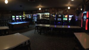 A dimly lit bar with multiple gaming machines, a pool table, and several tables and chairs. - Sharptail Motor (Ashern)