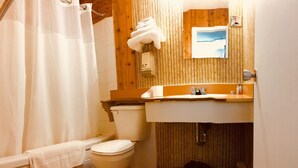 A bathroom with a wooden wall, a white sink, a toilet, and a shower curtain. - Sharptail Motor (Ashern)
