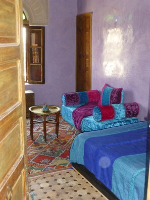 A room with a bed, a small table, and a patterned rug. - Dar Naima - Hostel (Fes)