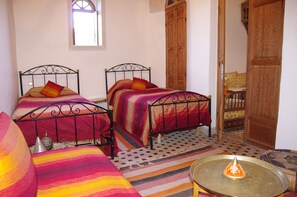 A room with two metal beds, a patterned rug, a small table with a candle, and a window. - Dar Naima - Hostel (Fes)
