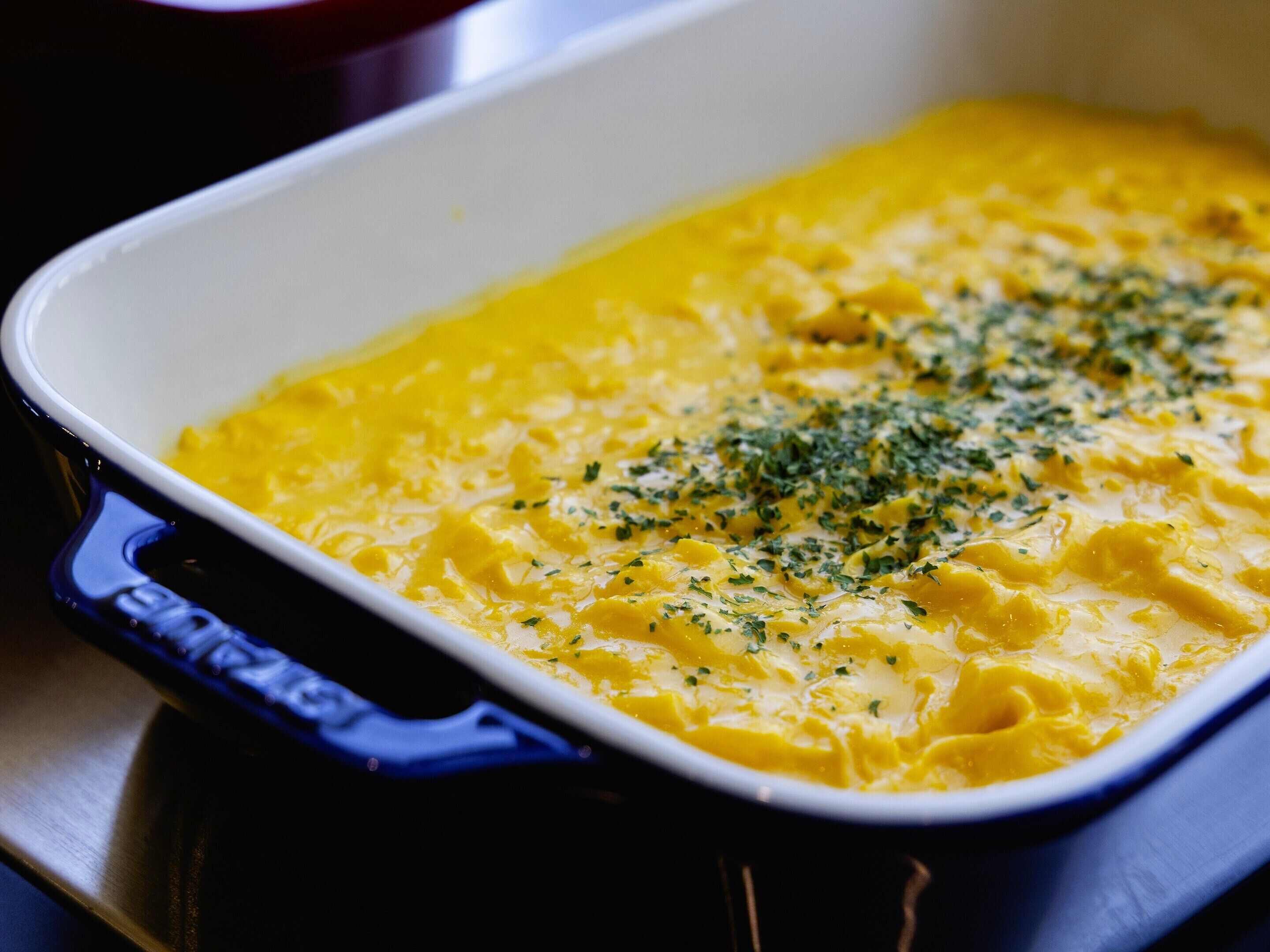 A blue baking dish with a yellow baked dish inside, garnished with green herbs.