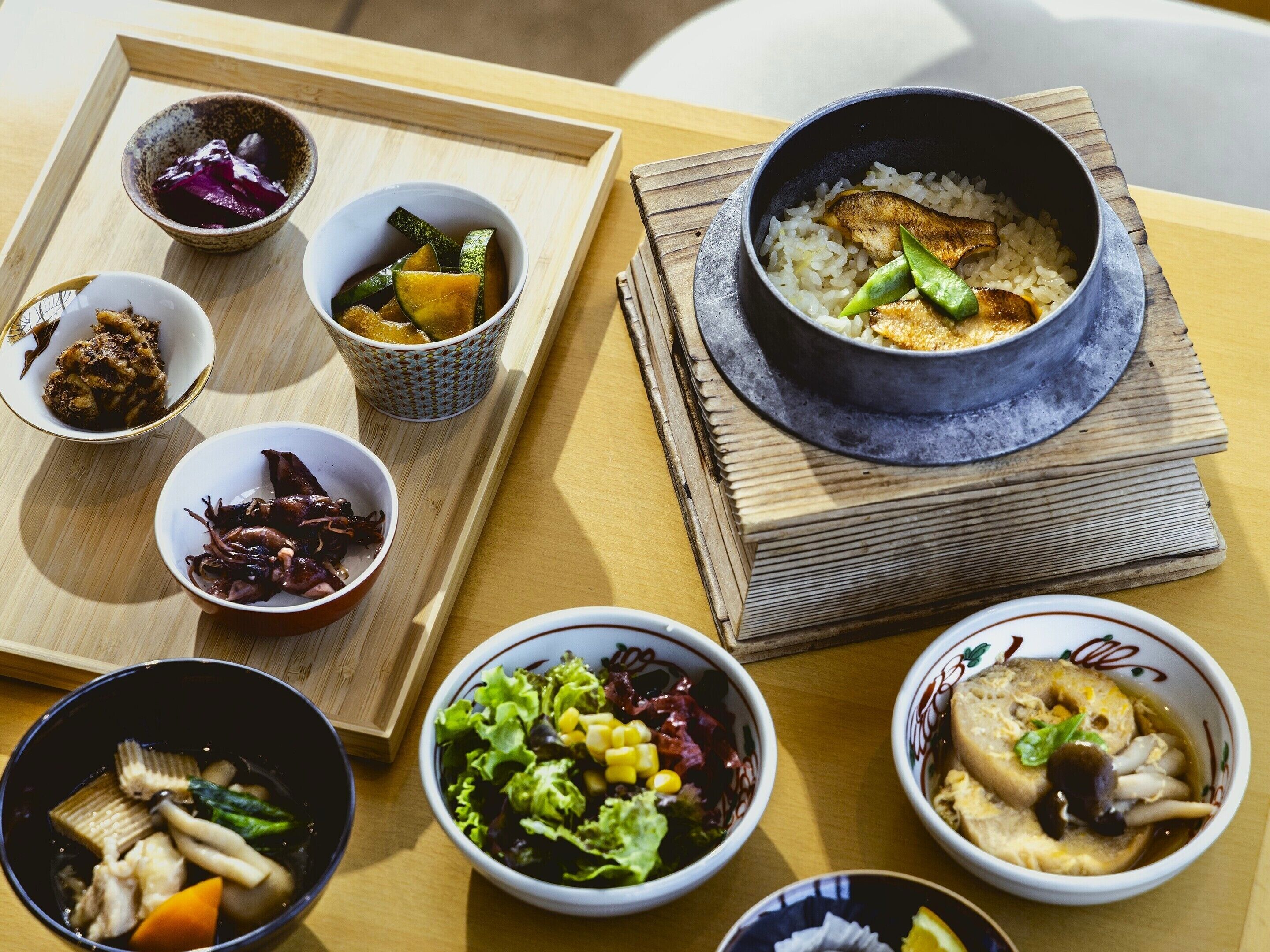 Une variété de plats sont disposés sur une table en bois, notamment des bols de riz, des légumes et de la viande.