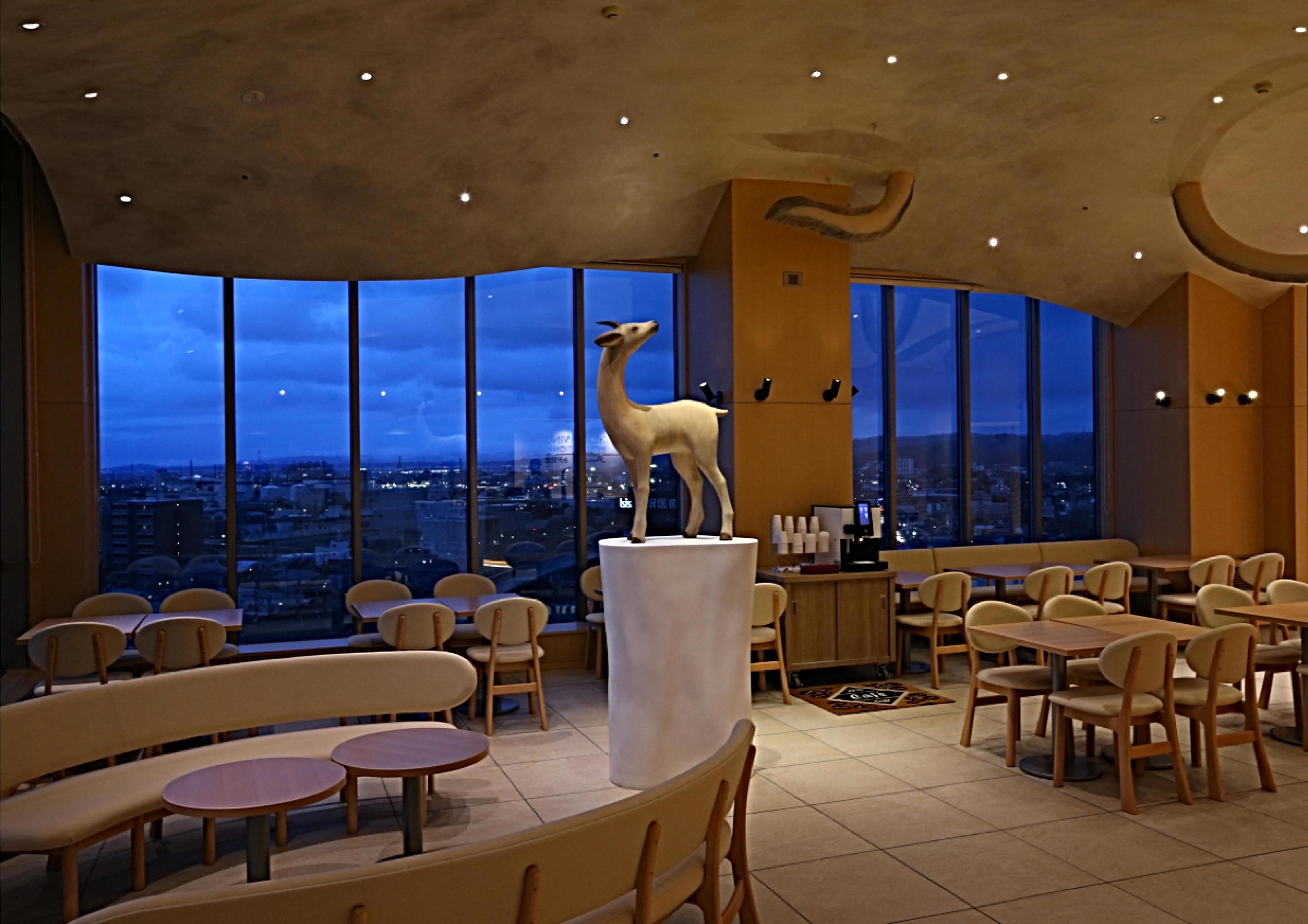 A restaurant with a large view of the city at night, featuring a giraffe sculpture on a pedestal.