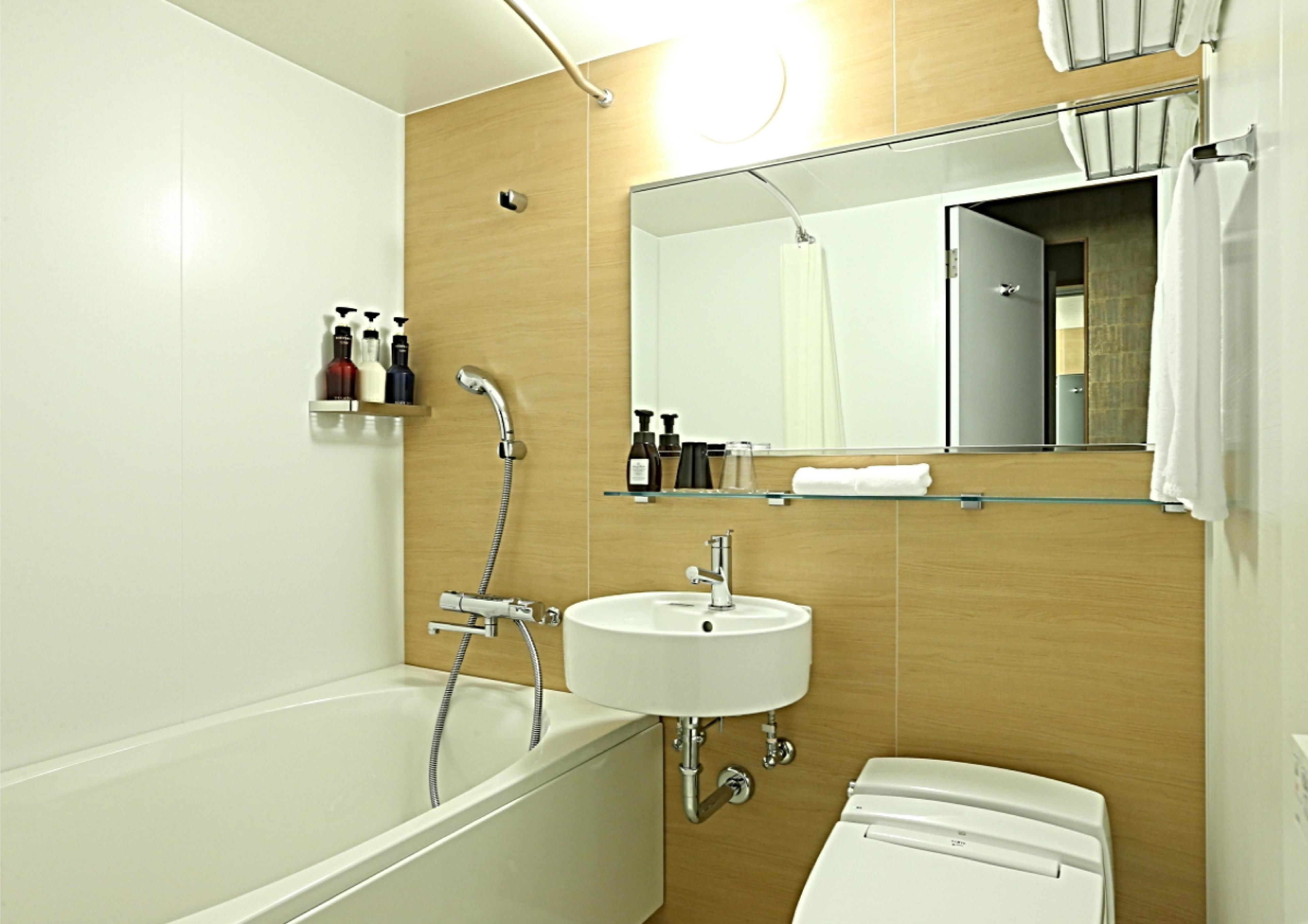 A modern bathroom with a bathtub, a sink, and a toilet. There is a mirror above the sink and a showerhead above the bathtub.