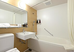 Un baño moderno con un lavabo blanco, espejo y bañera. Hay artículos de aseo en un estante y una barra de apoyo en la ducha.