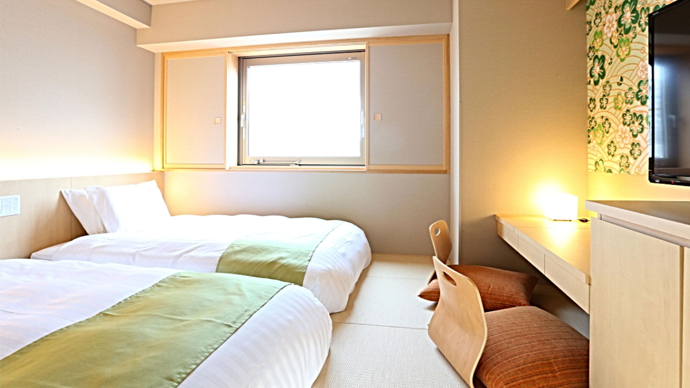 A hotel room with two beds, a window, a TV, and a desk.