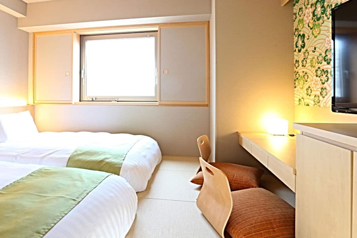 A hotel room with two beds, a window, a TV, and a desk.
