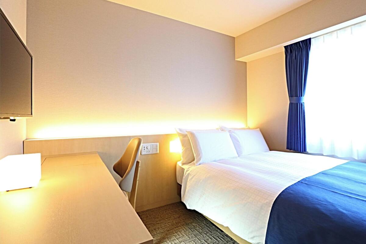 A hotel room with a bed, a desk, and a TV.