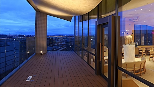 Un balcón moderno con suelo de madera, ventanas de vidrio amplias y vistas de la ciudad.