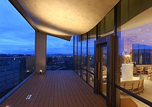 A modern balcony with a wooden floor, large glass windows, and a view of the cityscape. - KOKO HOTEL Kanazawa Station (Kanazawa)