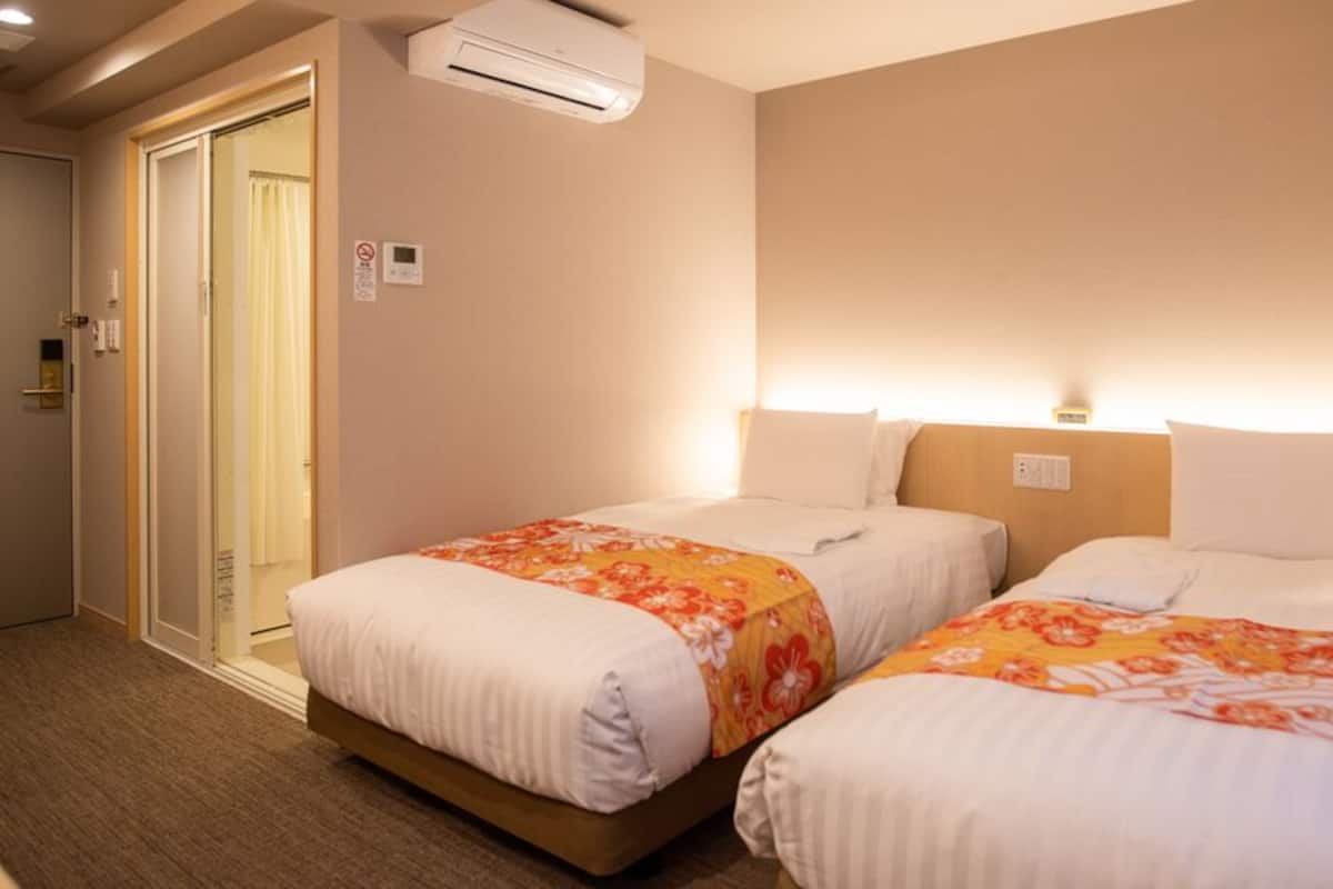 A hotel room with two beds, an air conditioning unit, a door, and a wall-mounted light fixture.