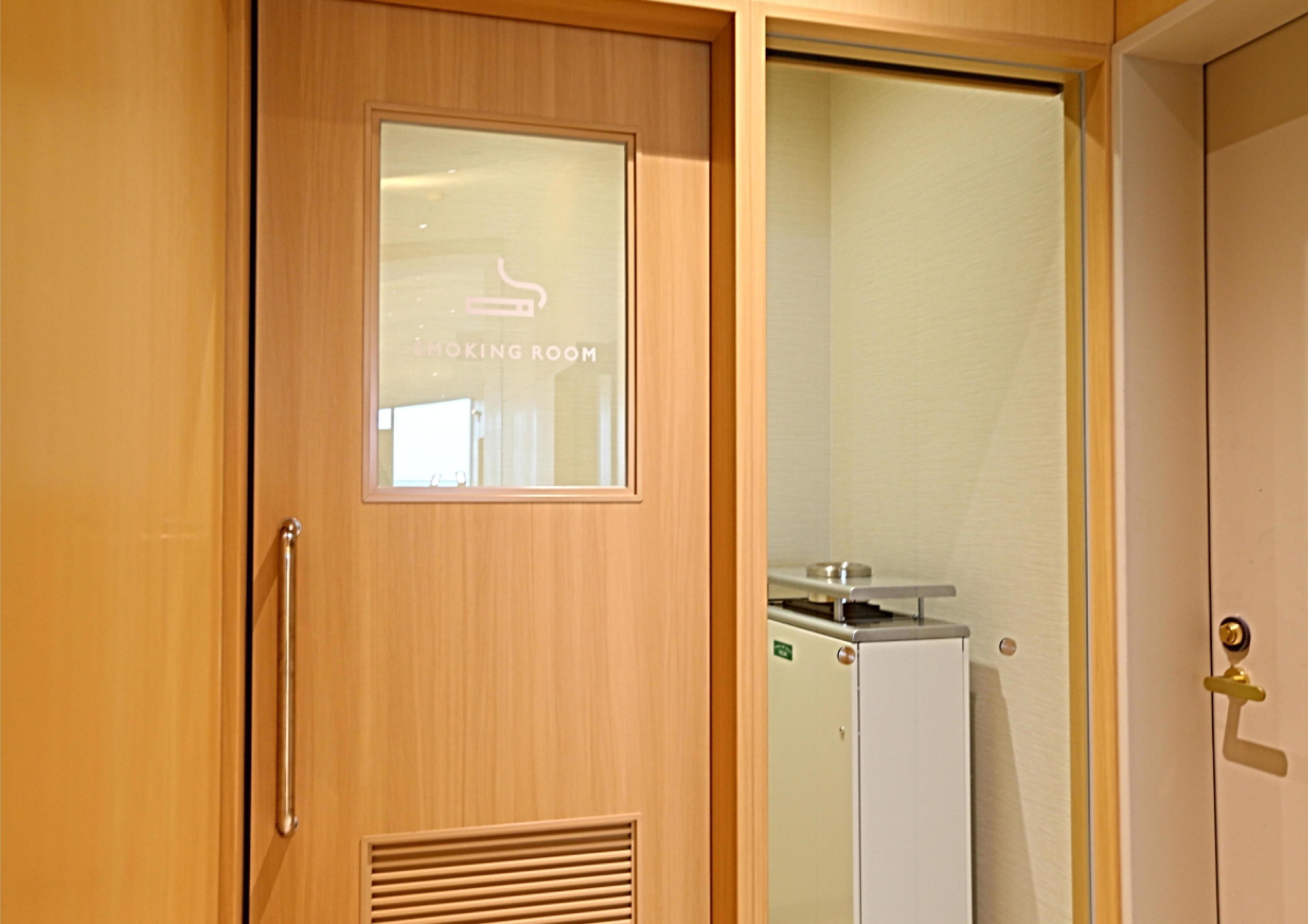 Una puerta de madera con un ventanal que indica "Smoking Room" y un pequeño calentador en la pared contigua.