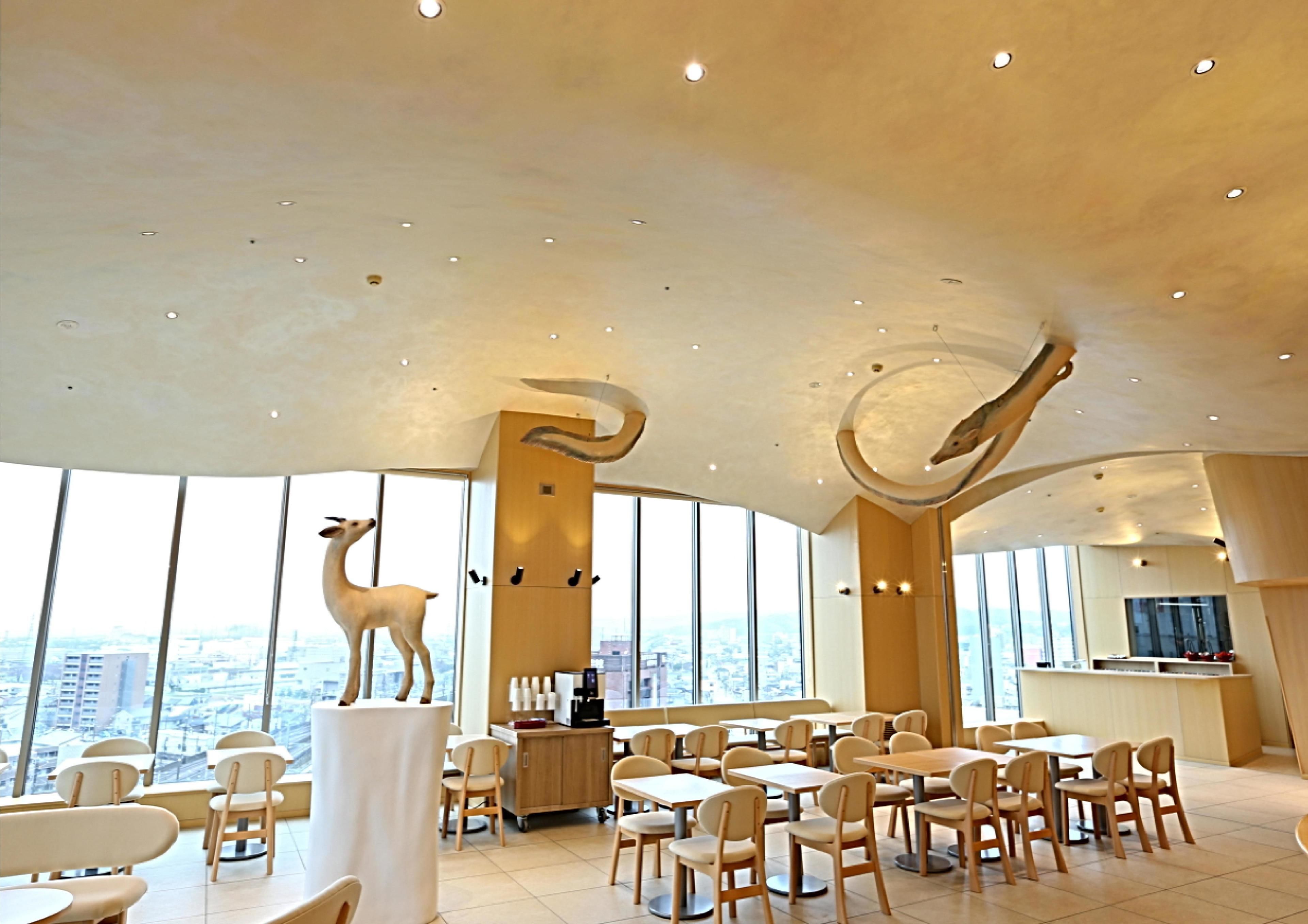 A spacious dining area with high ceilings, large windows offering city views, and a unique ceiling sculpture.