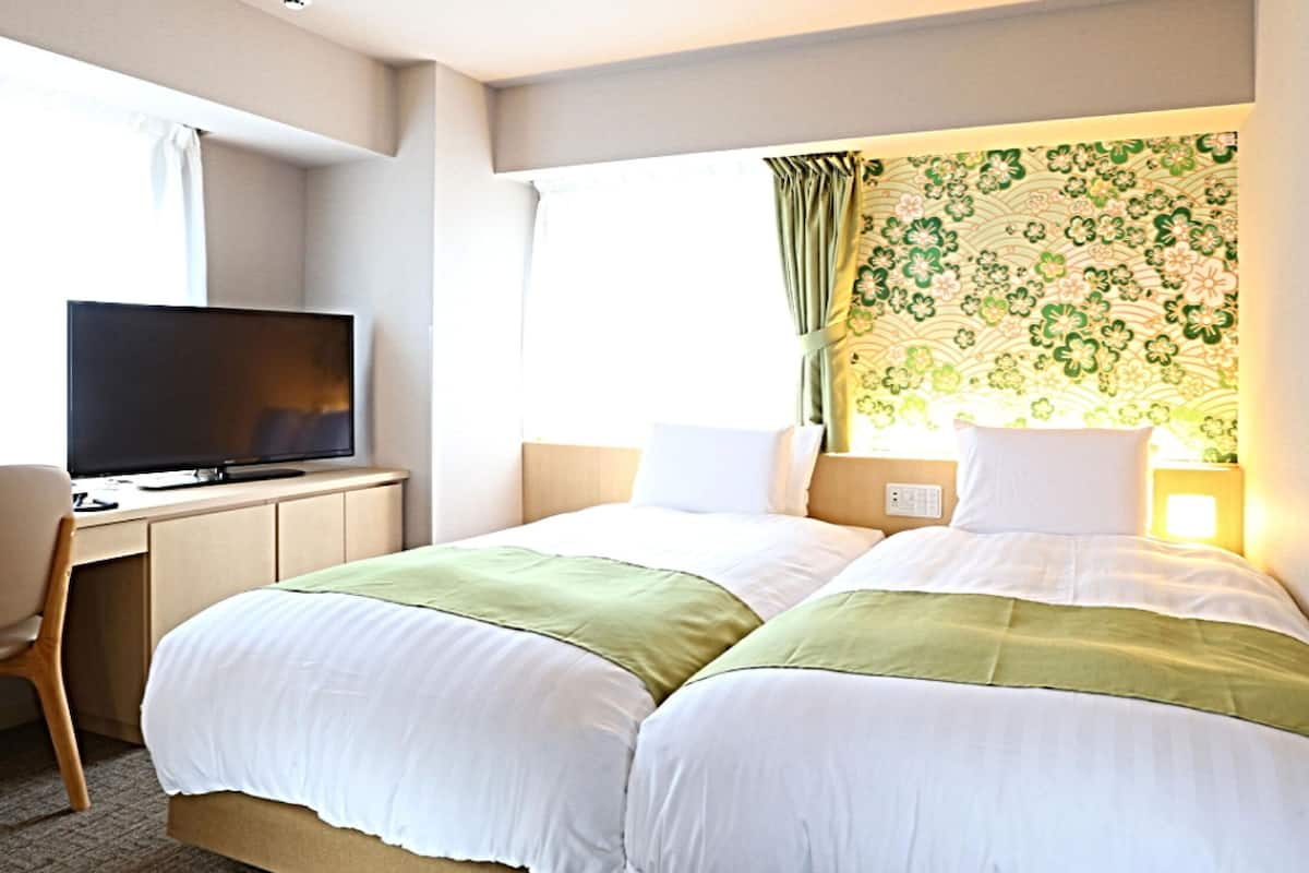A hotel room with two beds, a desk with a television, and a window with curtains.