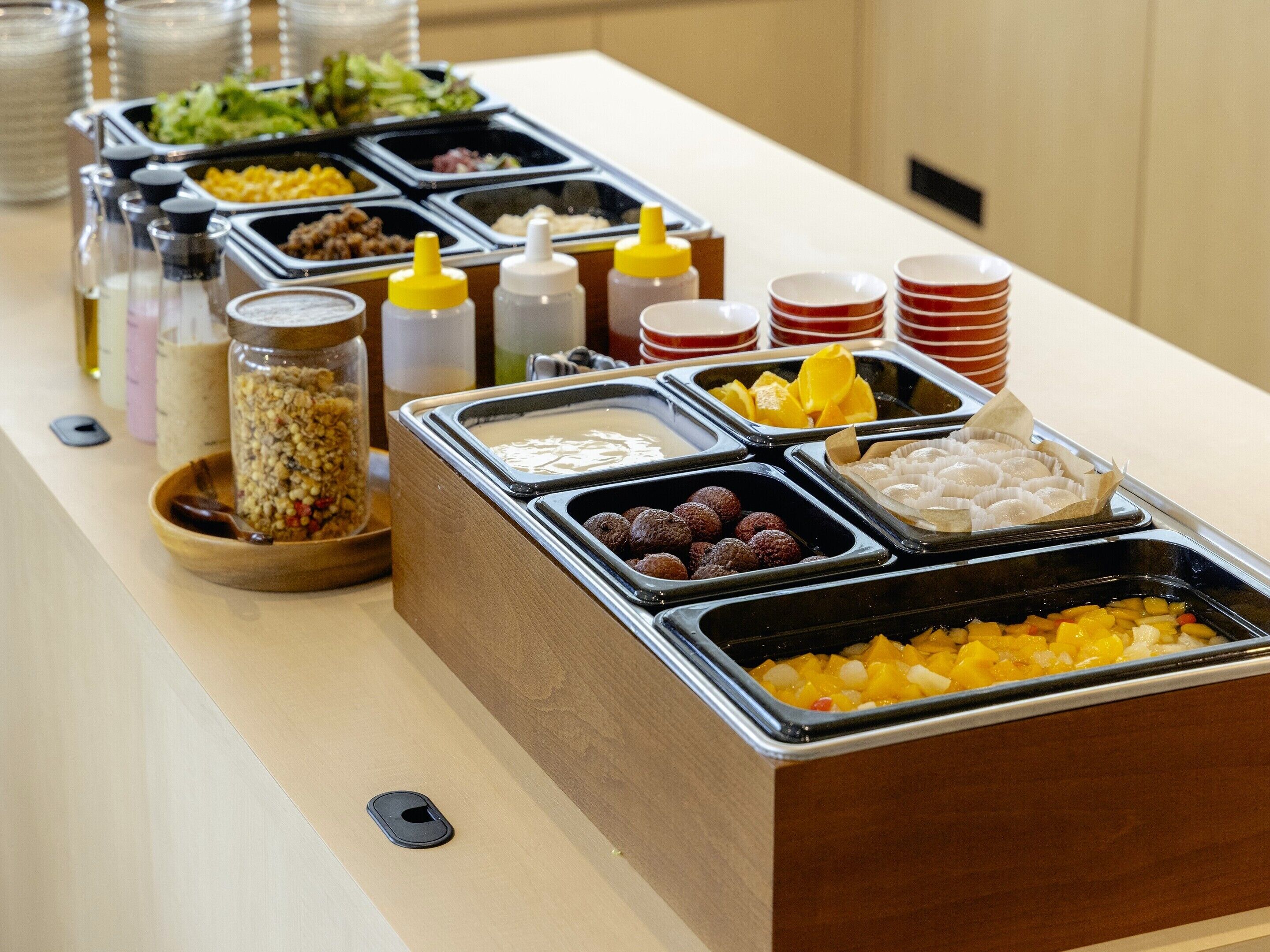A buffet with various food options including fruits, pastries, and condiments.