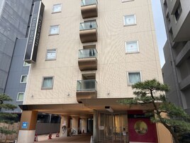 Un hotel con fachada moderna, varios balcones y una entrada despejada.