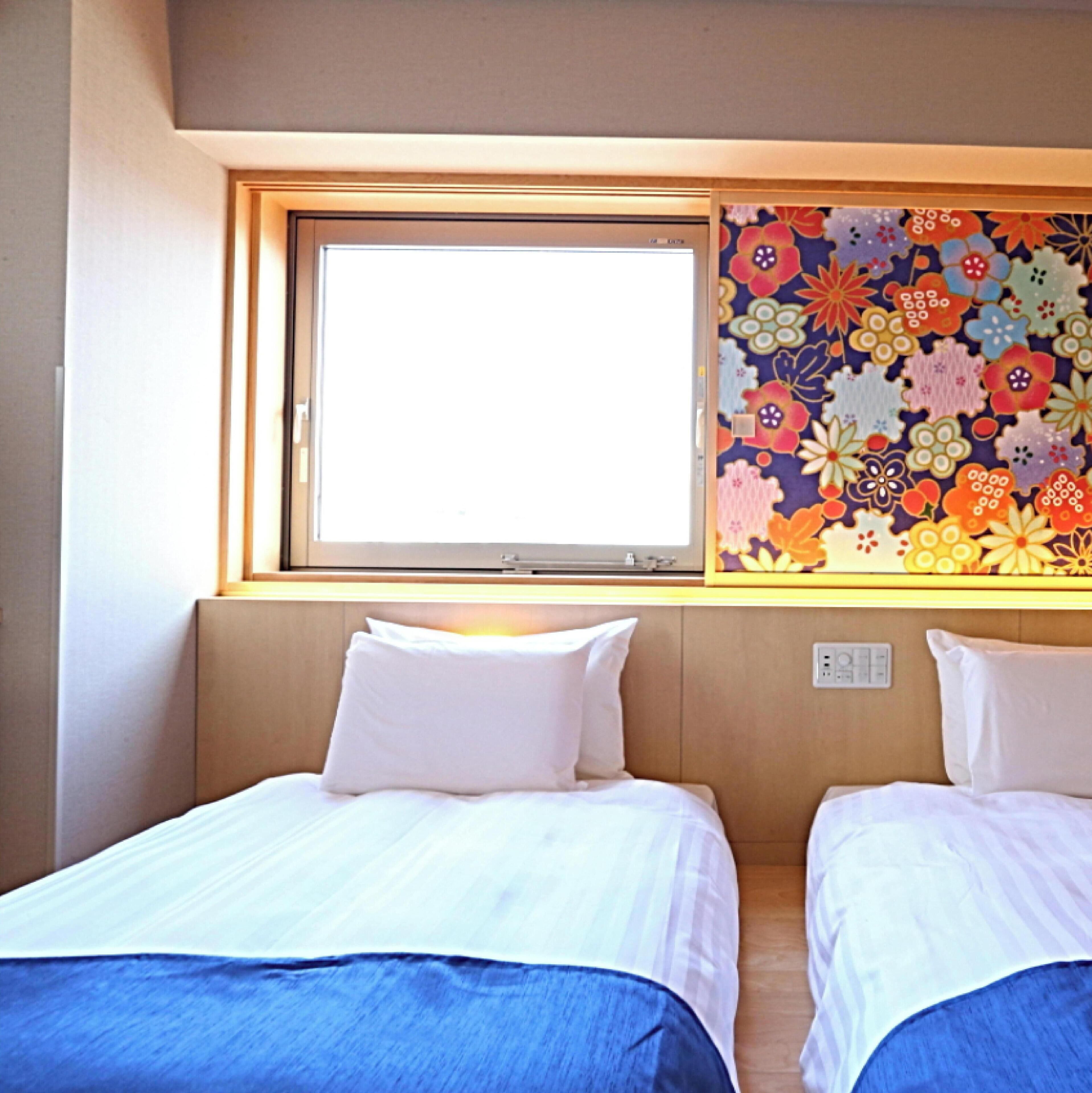 A hotel room with two beds, a window with a view, and a floral-patterned wall.