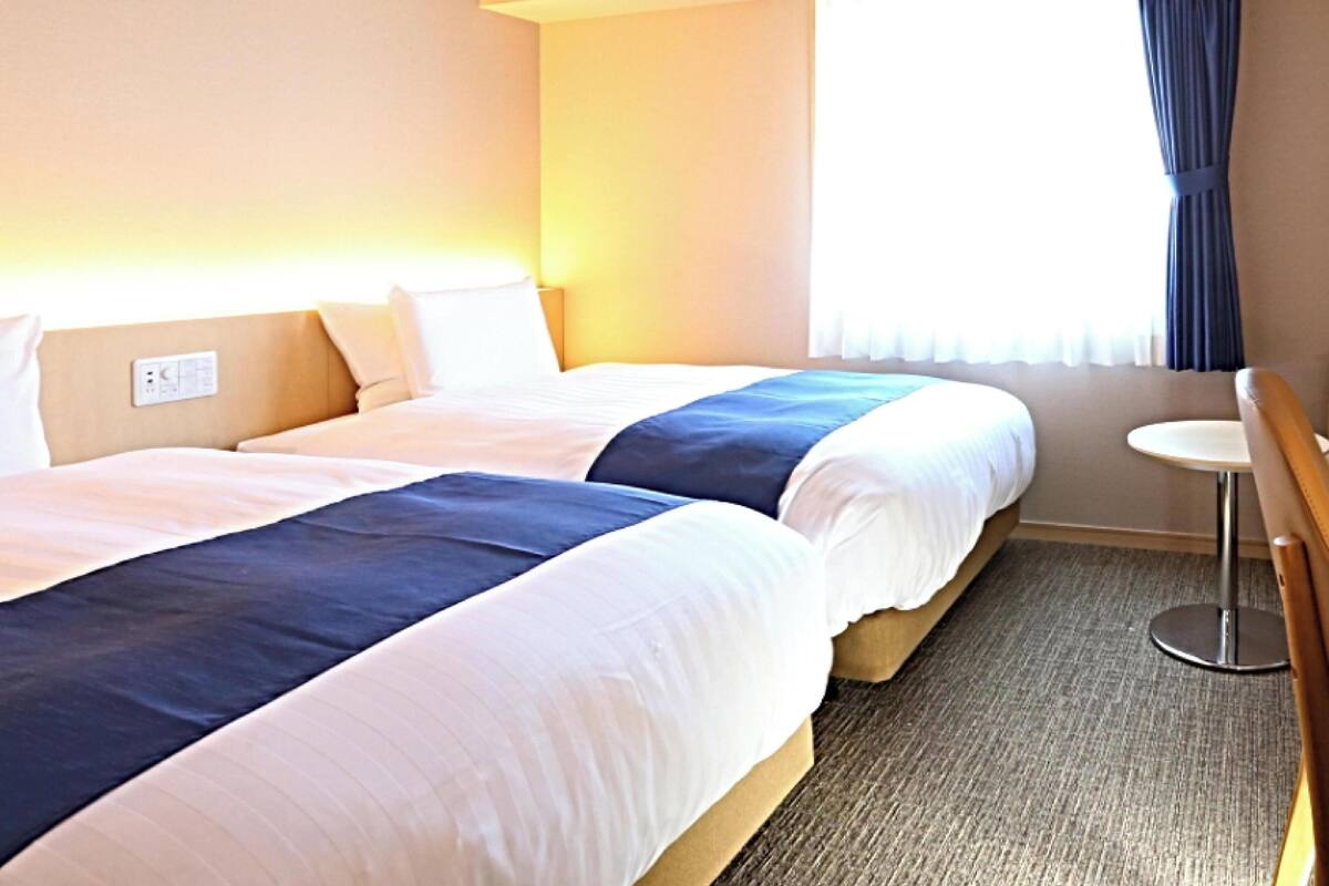 A hotel room with two beds, a small table, and a window with curtains.