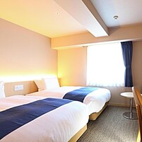 Habitación de hotel con dos camas, una mesita y una ventana con cortinas.