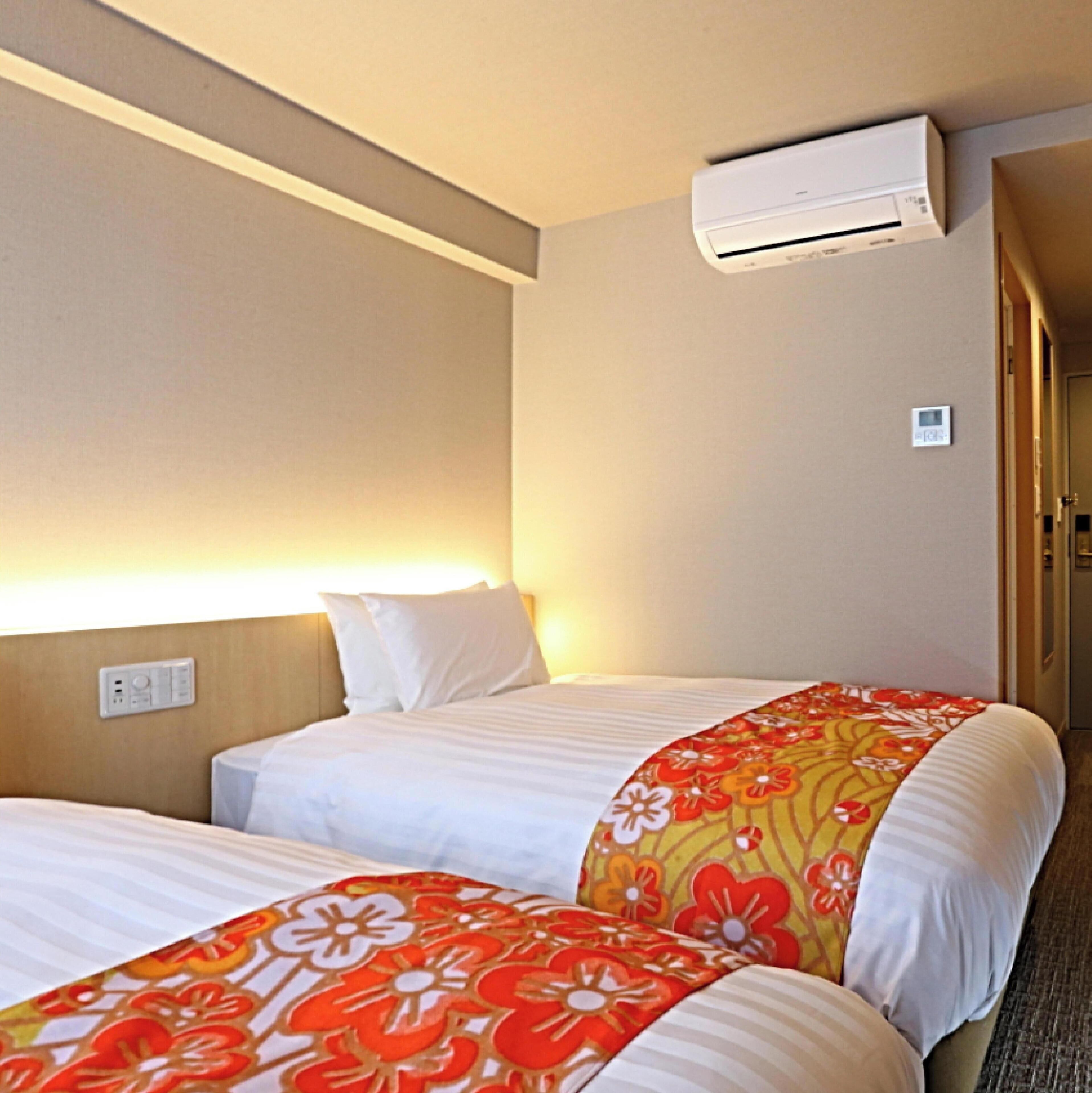Una habitación de hotel con dos camas, aire acondicionado en la pared y una mesita de noche con lámpara.