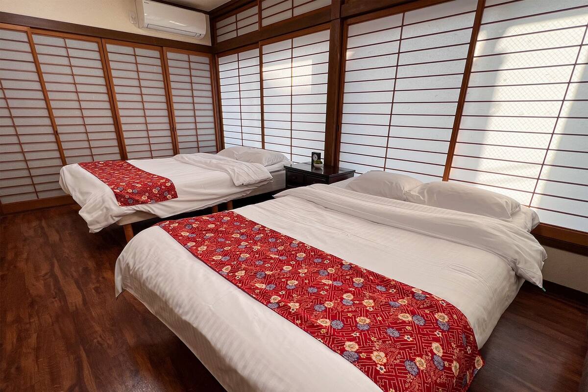 A traditional Japanese-style room with tatami flooring, two beds with red and white bedding, and shoji screens.