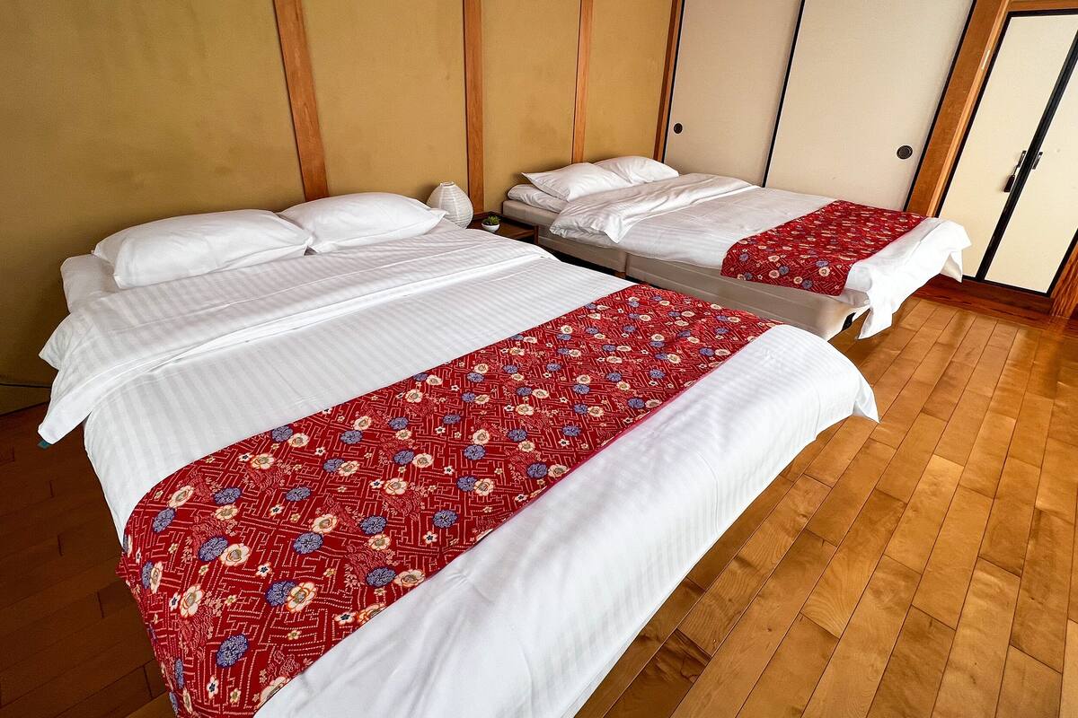 Two beds with white linens and red floral bedspreads in a room with wooden flooring and traditional sliding doors.