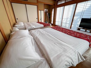 A hotel room with two beds, wooden flooring, a TV, and large windows with blinds. - Hondori Inn (Hiroshima)
