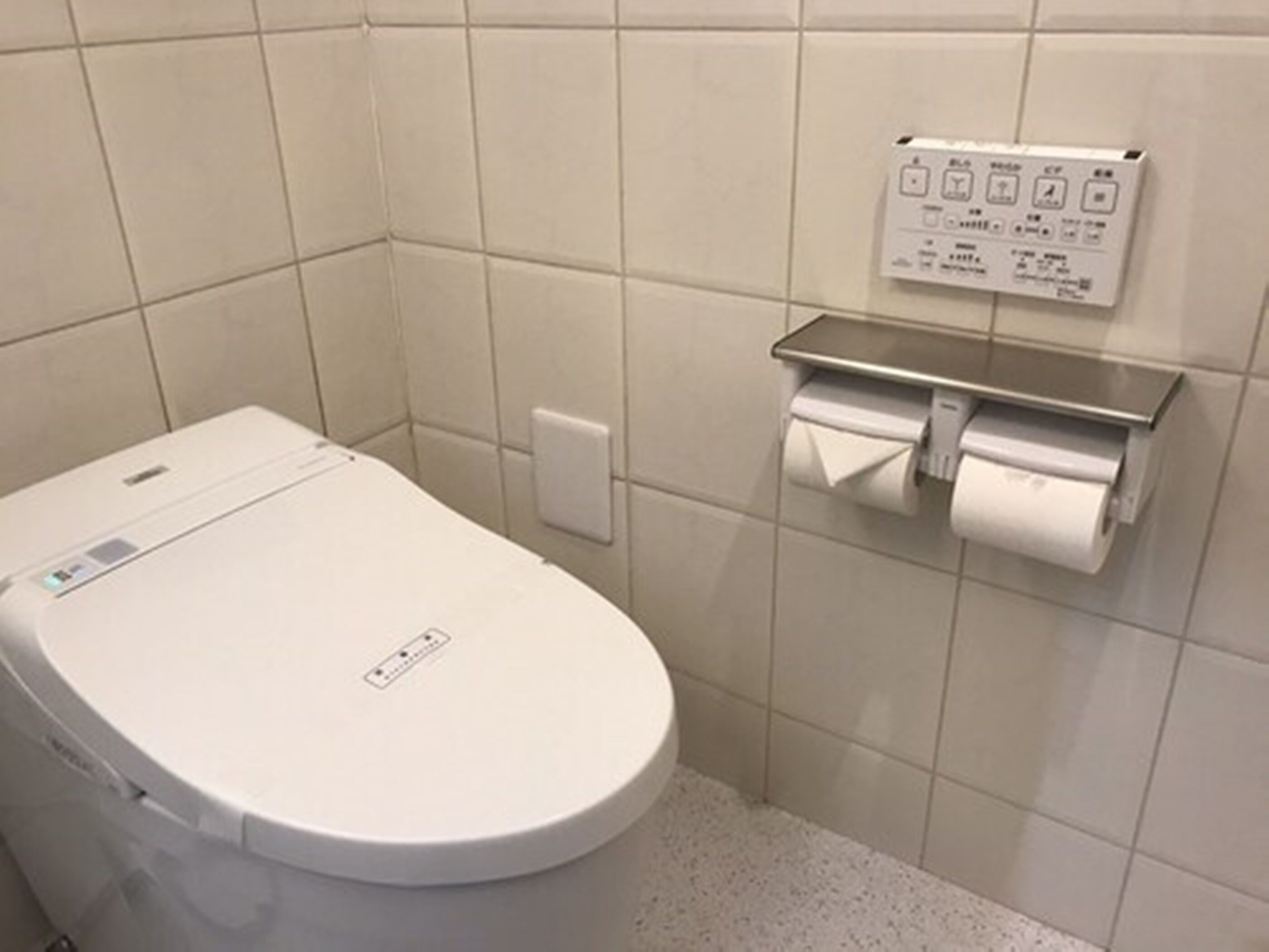 A modern toilet with a control panel, a paper towel dispenser, and a flush button.