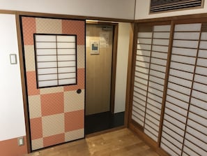 Ein Zimmer mit einer gleitenden Shoji-Schiebetür, Holzboden und einem kleinen Fenster mit Jalousien.