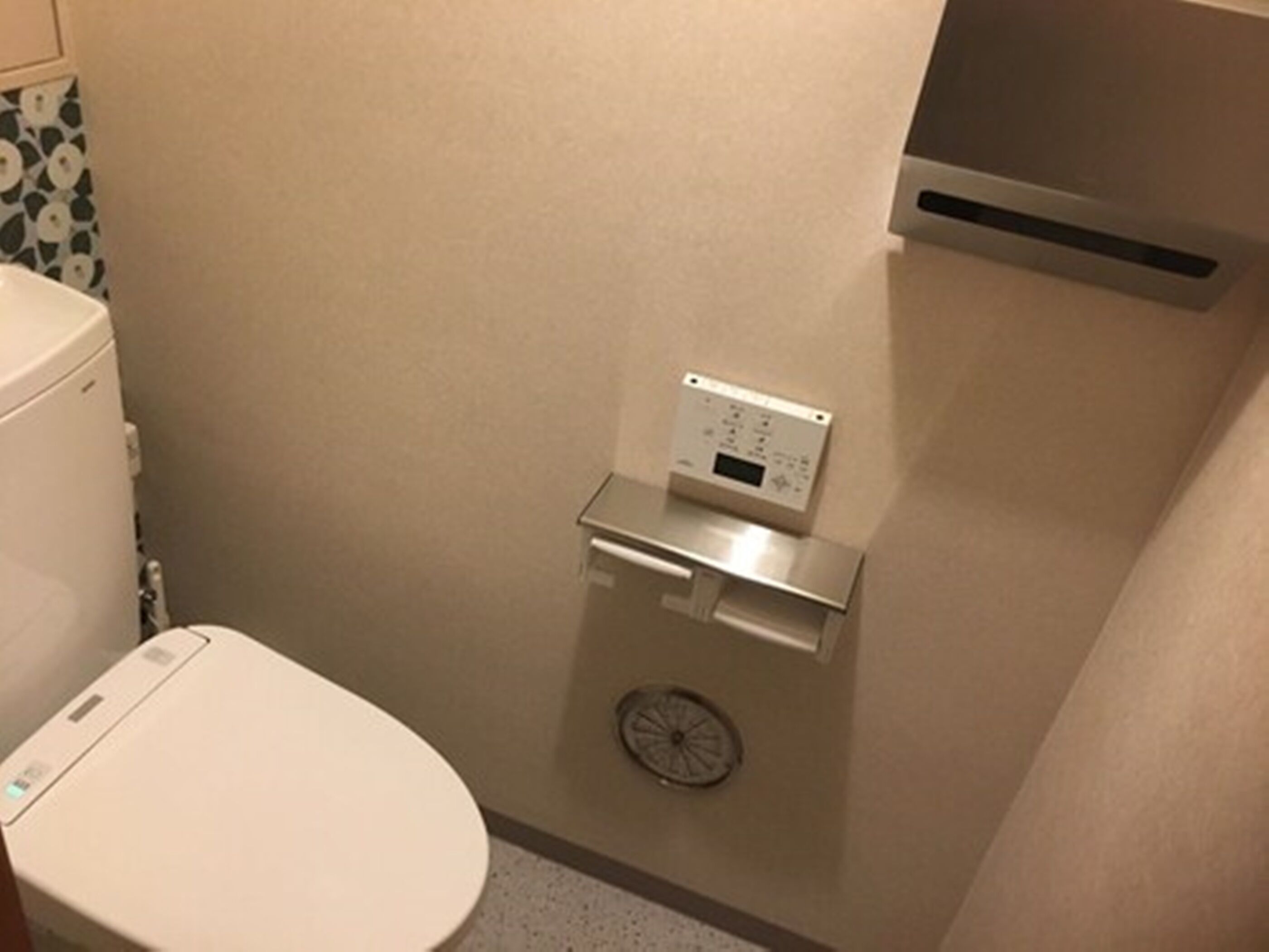 A bathroom with a toilet, a wall-mounted scale, and a vent.
