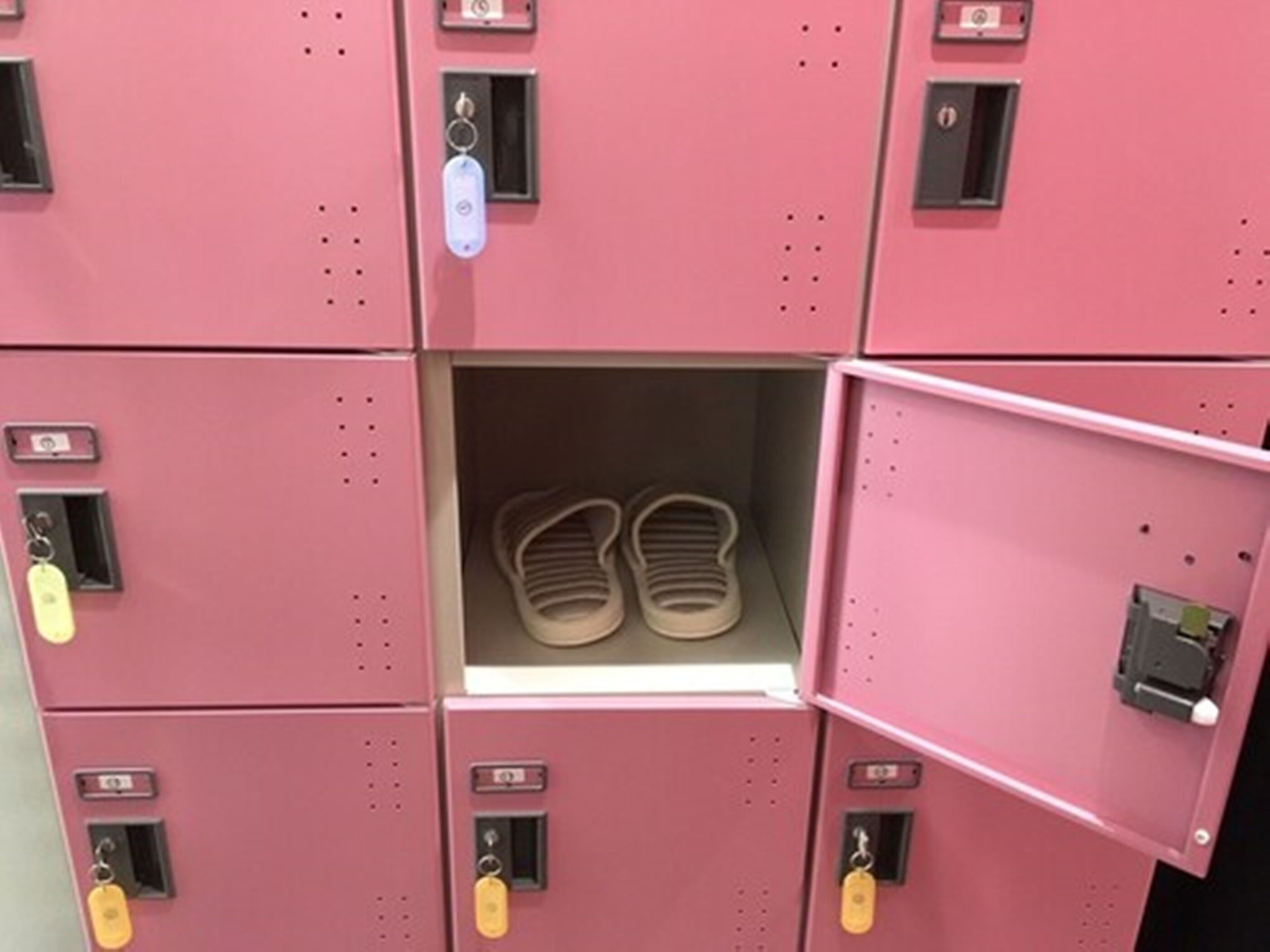 A row of pink lockers with a single open locker containing a pair of sandals.