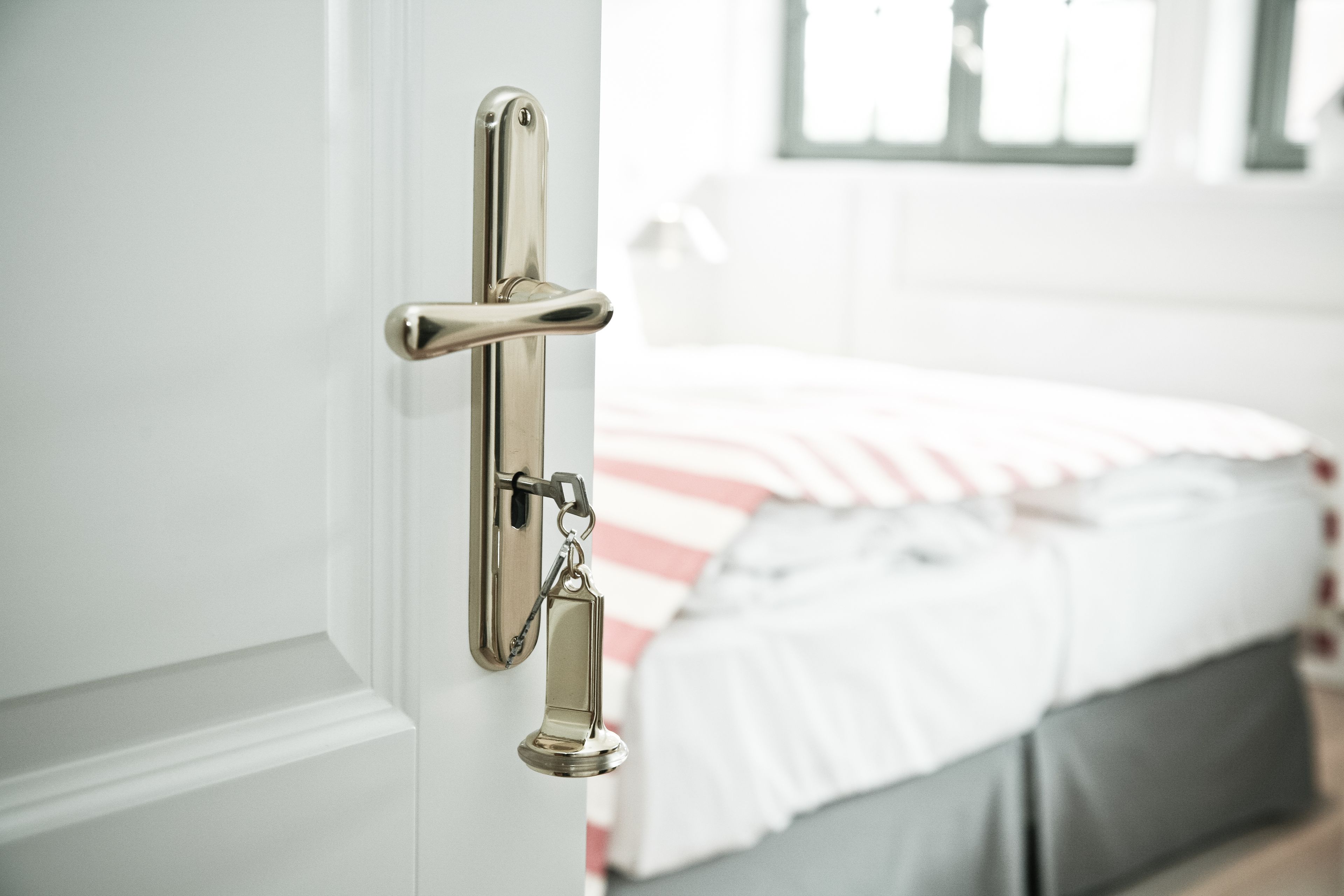 A door with a silver handle and a keychain, leading to a bedroom with a bed and a window.