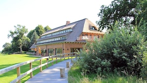 A large brick building with a wooden deck leading to a gated entrance. - Landhaus Töpferhof (Ratekau)