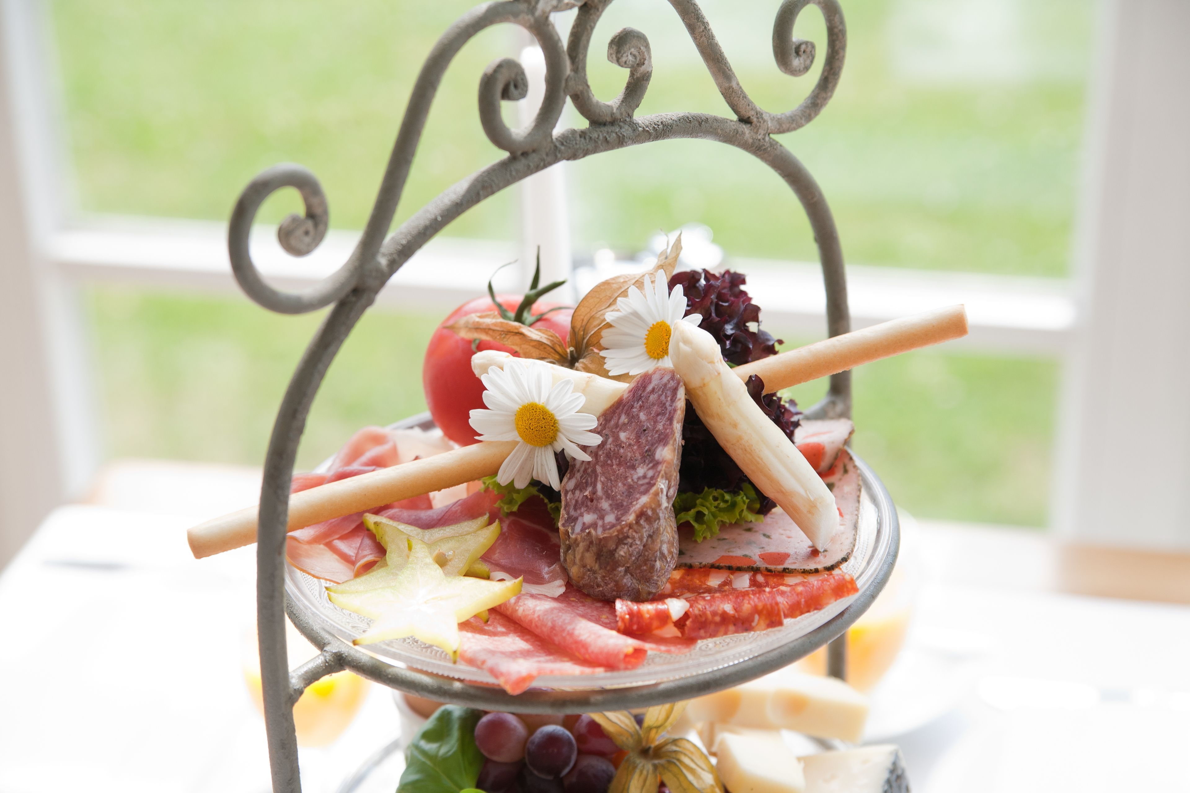 Una tabla de embutidos con varios tipos de carne, quesos y frutas sobre un soporte de metal.