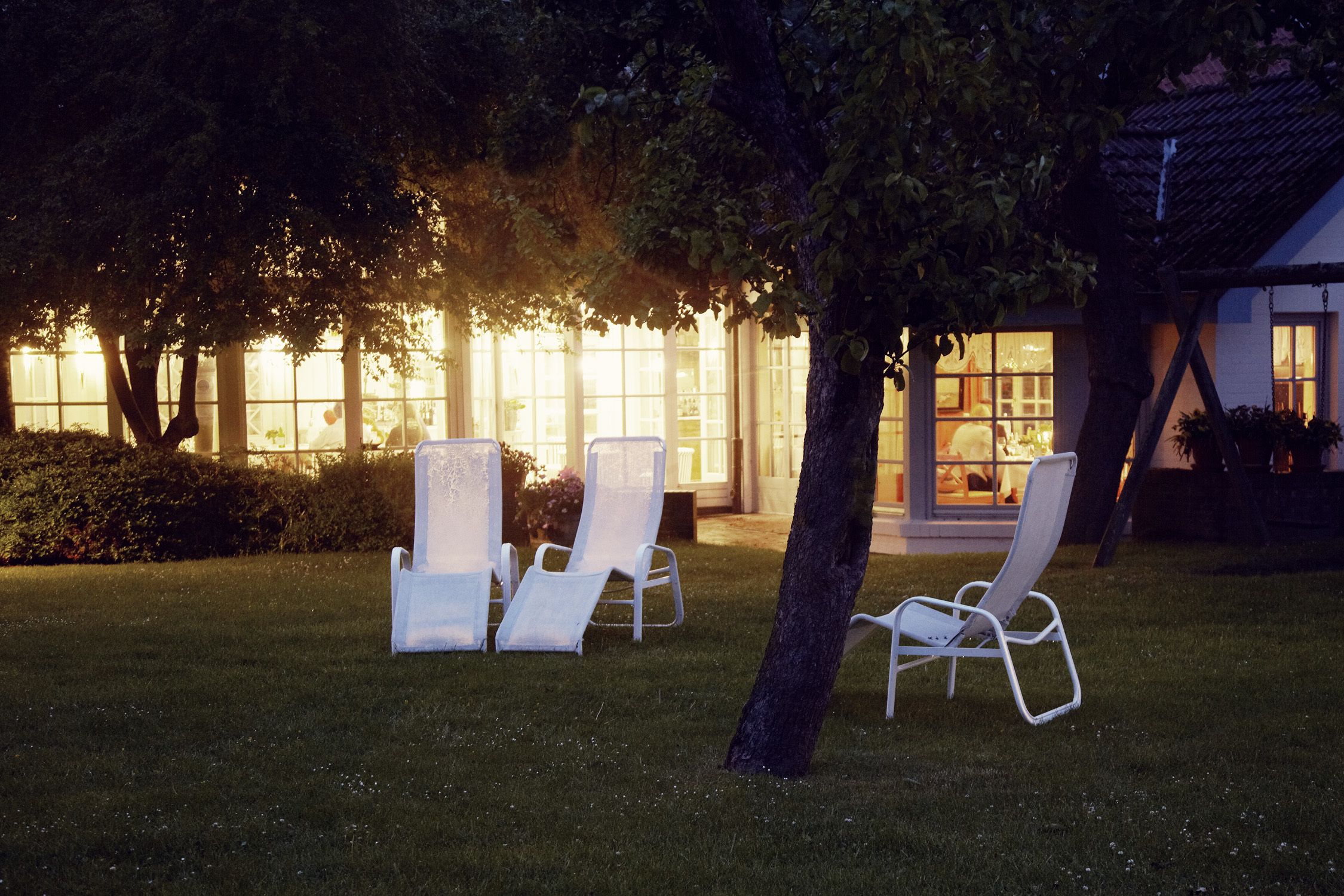 A garden with two white lounge chairs and a building with large windows in the background.