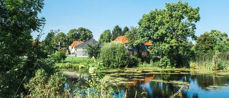 Et roligt sølandskab med et hus, der har rødt tag og hvide vægge, omgivet af frodig vegetation og træer.
