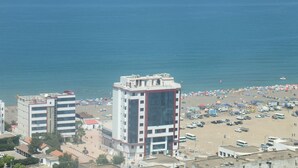 A hotel with multiple floors, a beach in the background, and a parking area with several vehicles. - Hotel Syphax (Bejaia)