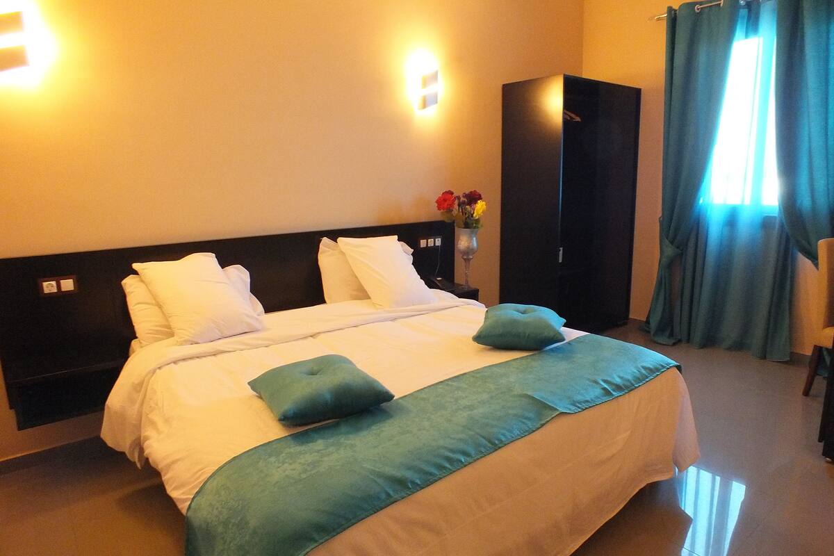 A hotel room with a large bed, a wardrobe, and a window with curtains.