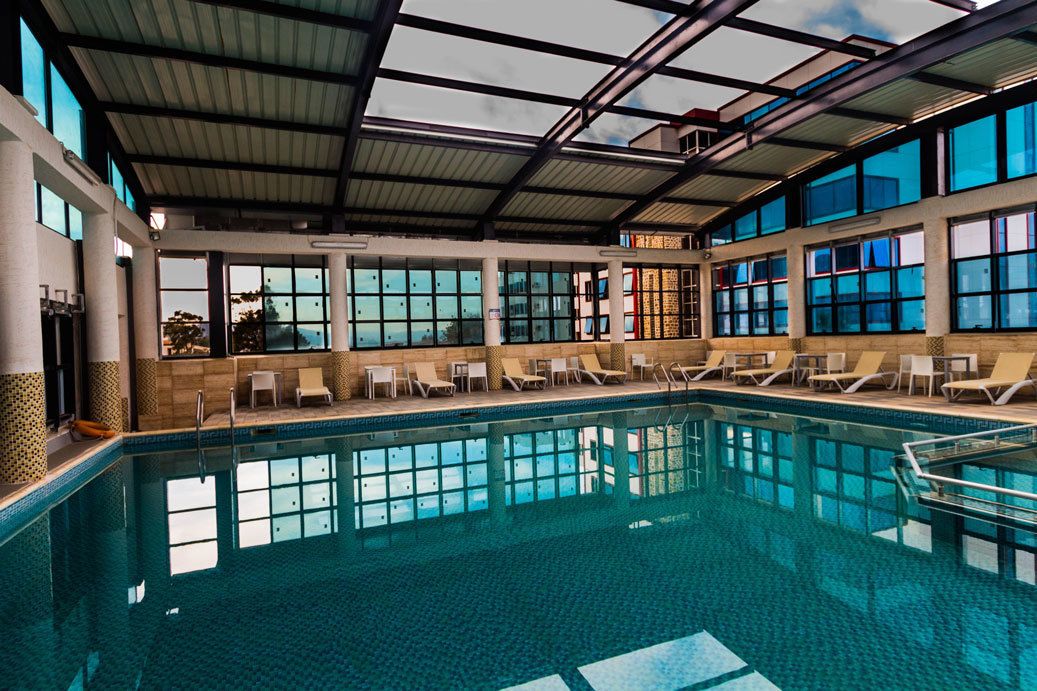 Una piscina techada, una piscina al aire libre, sombrillas