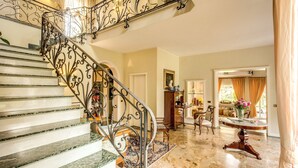 Una gran escalera con barandillas de metal ornamentadas, piso de mármol y un comedor con mesa y sillas.