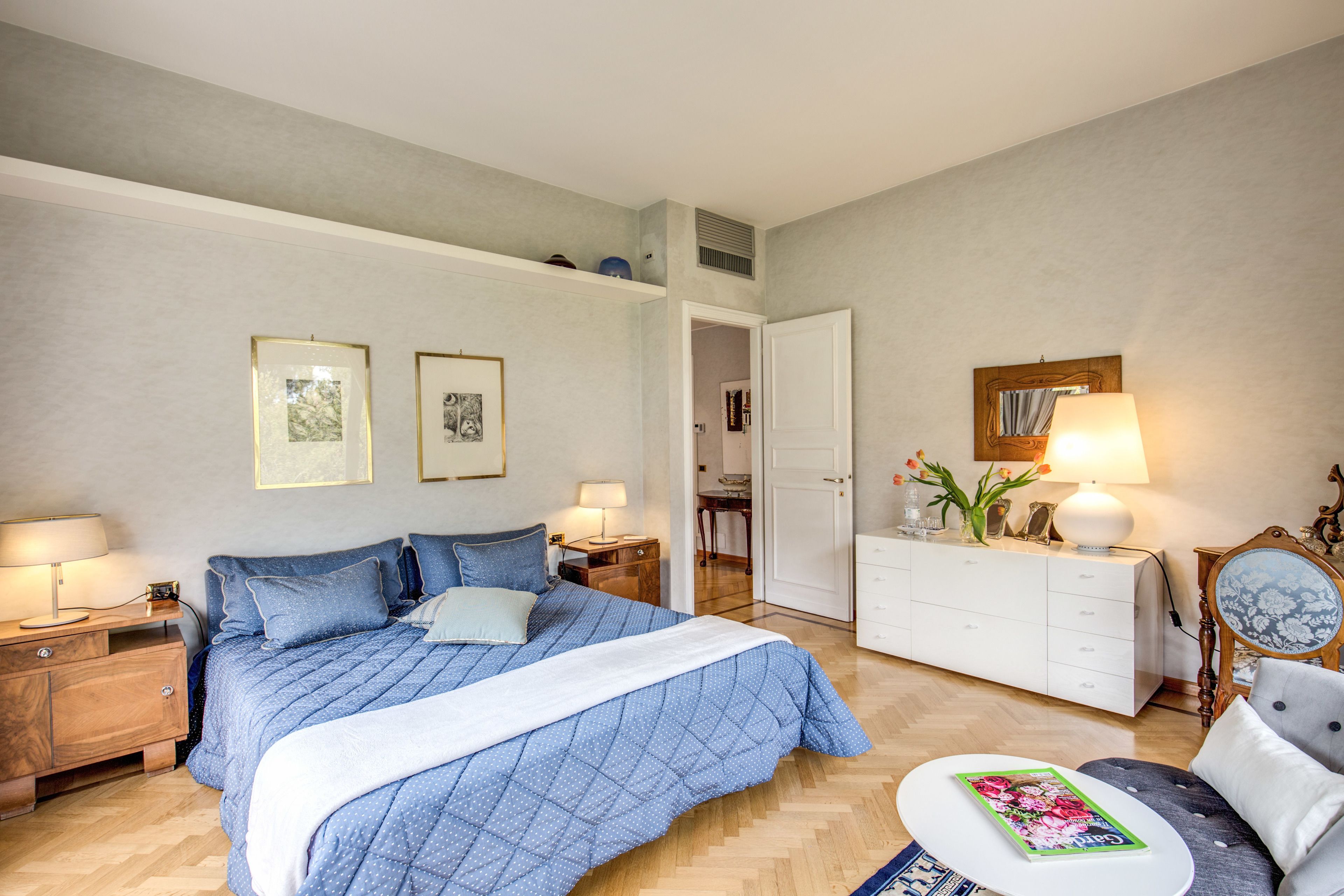 Un dormitorio con una cama grande, un aparador, una silla y una mesita de noche. Hay dos cuadros en la pared.