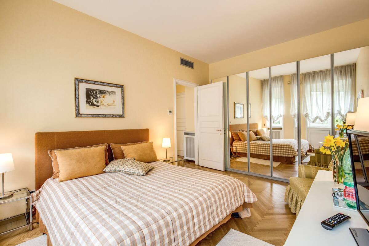 Ein Hotelzimmer mit einem großen Bett, einem Schreibtisch mit Computer und Fernbedienung, einem Spiegel und einem gerahmten Bild an der Wand.
