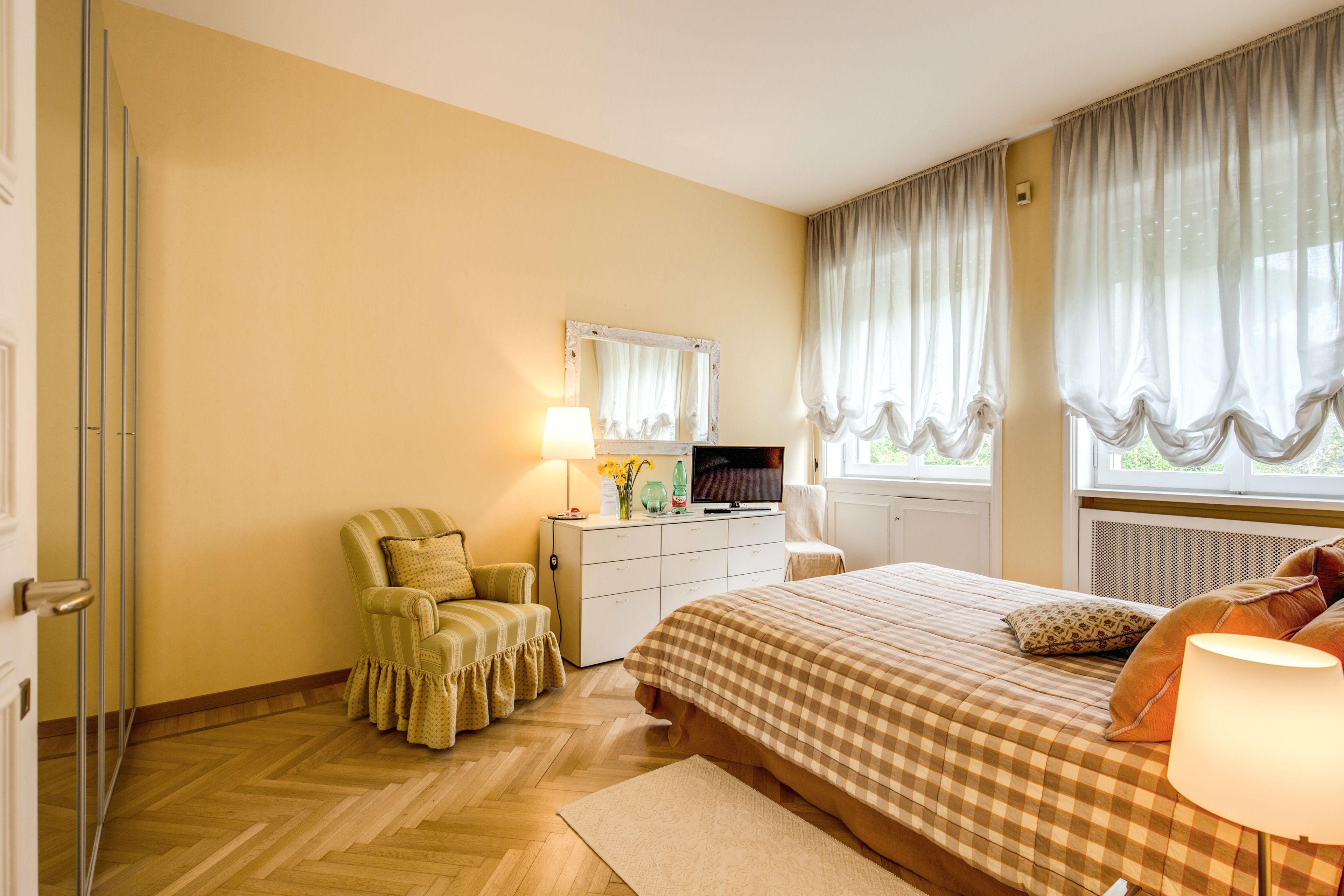 A bedroom with a bed, a chair, a dresser, a television, and a window with curtains.